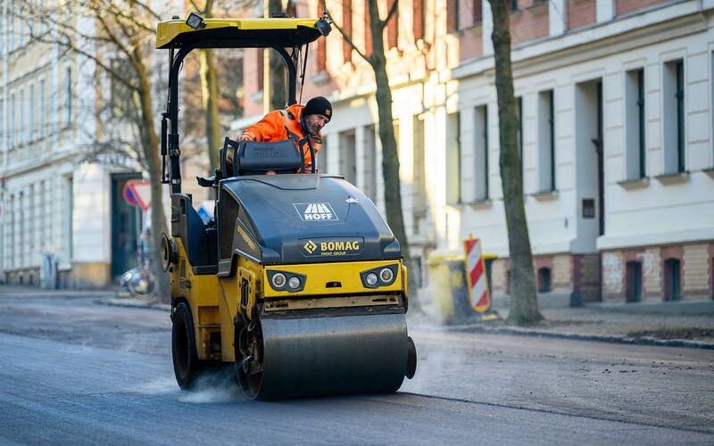 Baustellenfotografie in Sachsen: Eine tonnenschwere Walze bei der präzisen Verdichtung der frischen Asphalttragschicht.