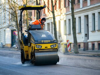 Baustellenfotografie in Sachsen: Eine tonnenschwere Walze bei der präzisen Verdichtung der frischen Asphalttragschicht.