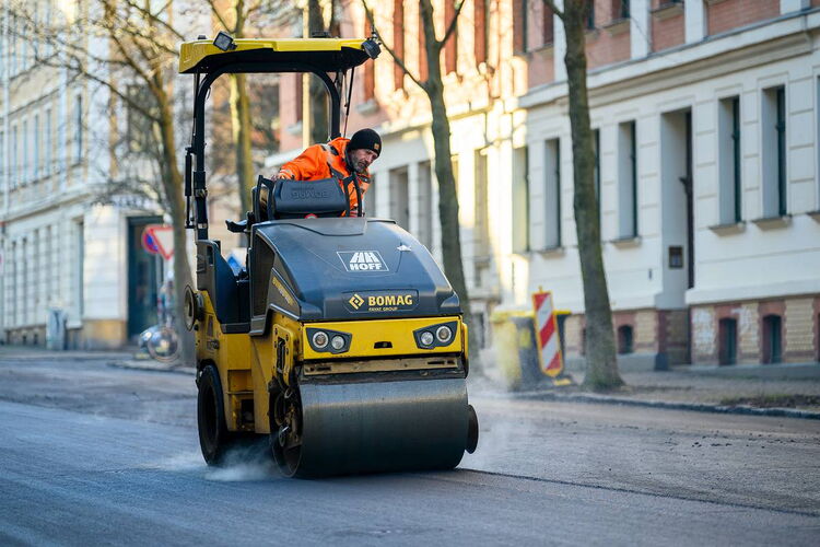Baustellenfotografie in Sachsen: Eine tonnenschwere Walze bei der präzisen Verdichtung der frischen Asphalttragschicht.