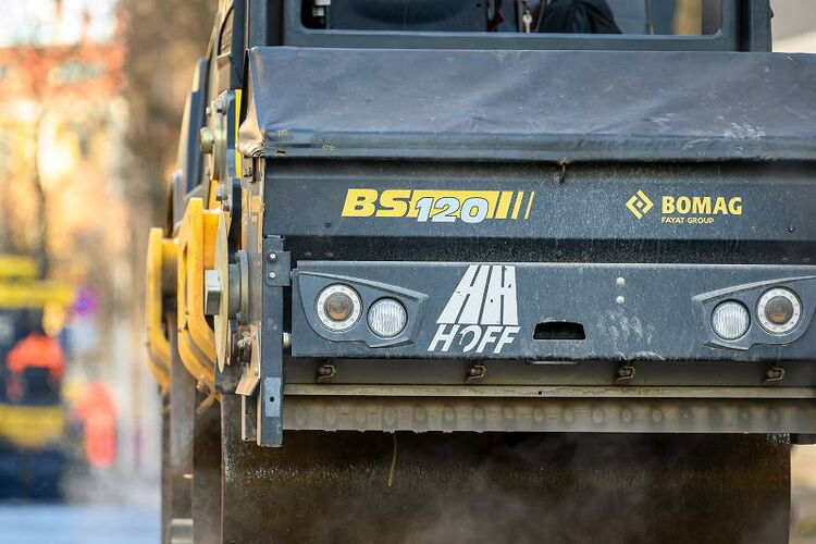 Authentisches Mitarbeiterfoto im Straßenbau: Ein Facharbeiter bei der konzentrierten Kontrolle des Asphalteinbaus in Leipzig.